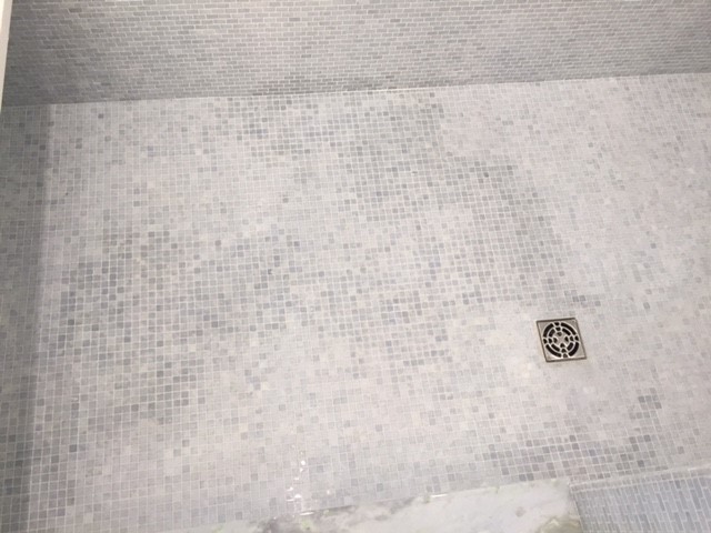 Shower floor tile discoloration extending up the wall